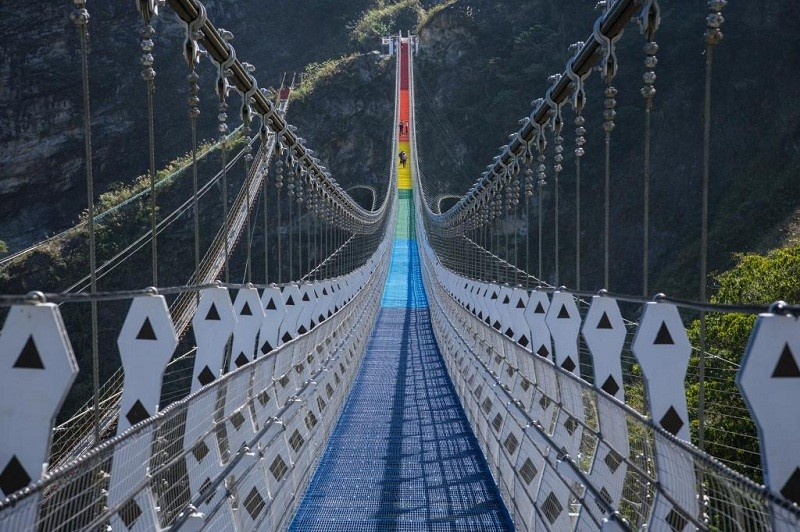 The more Modern \"Rainbow\" suspension bridge between mountain peaks.